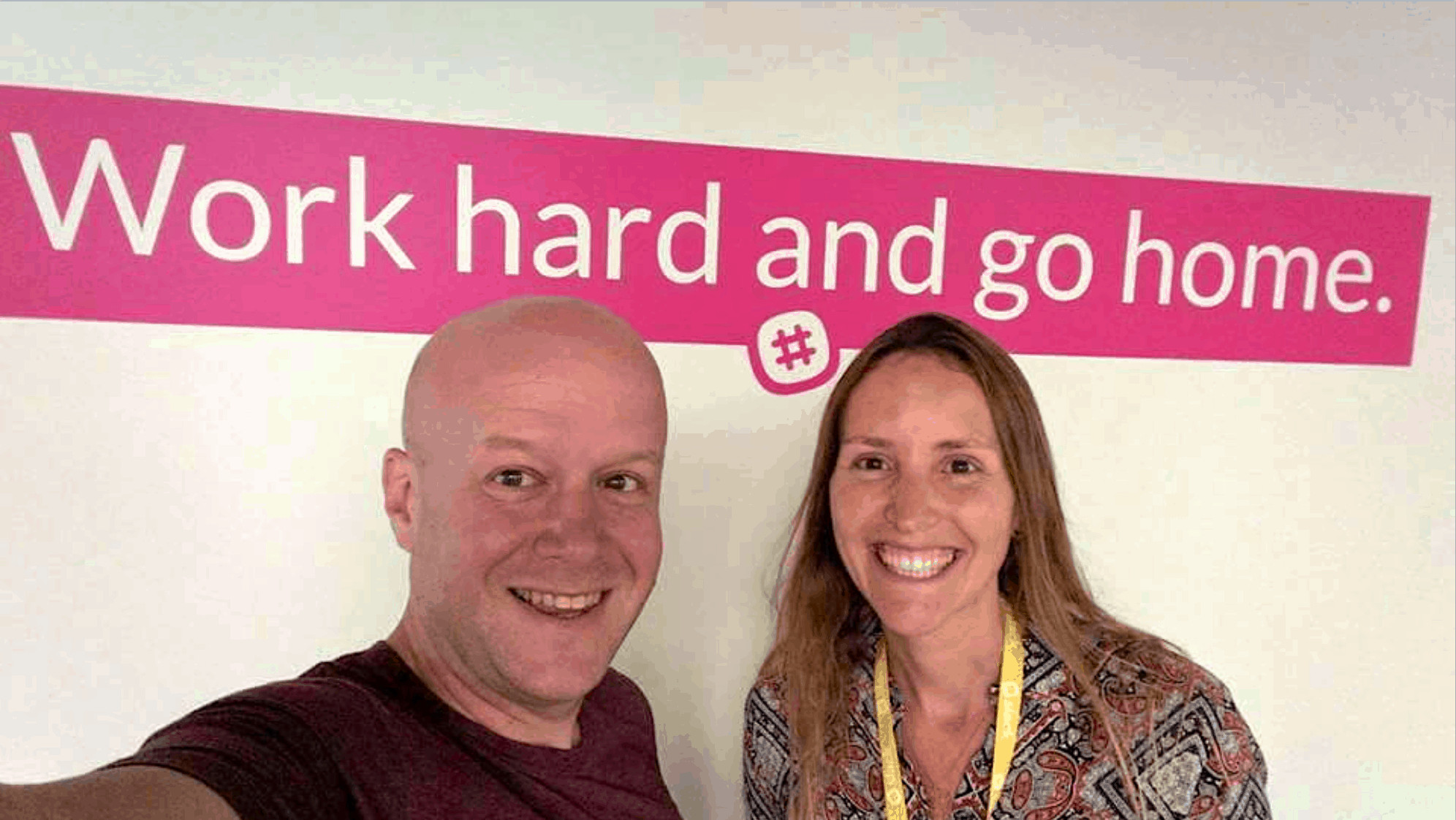 Young man and woman smiling in front of work hard and go home sign