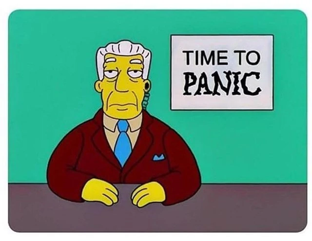 Kent Brockman of the Simpsons faces audience stoically next to a sign that says it is time to panic